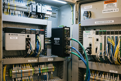 Industrial edge computing gateway connected to Allen-Bradley ControlLogix and Schneider Modicon PLC racks in an industrial automation cabinet